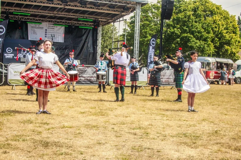 Highland dancers performing in front of an outdoor stage while the band plays