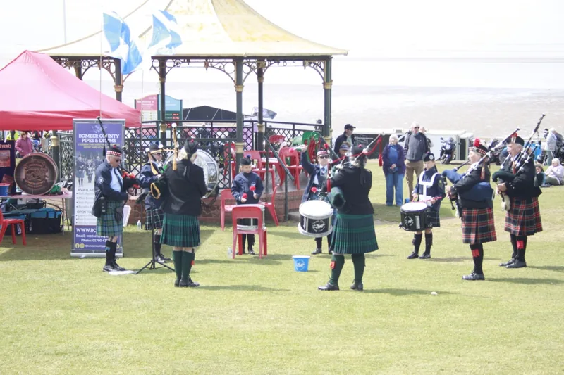 The band playing in a circle on a showground beside a bandstand and Saltire flags