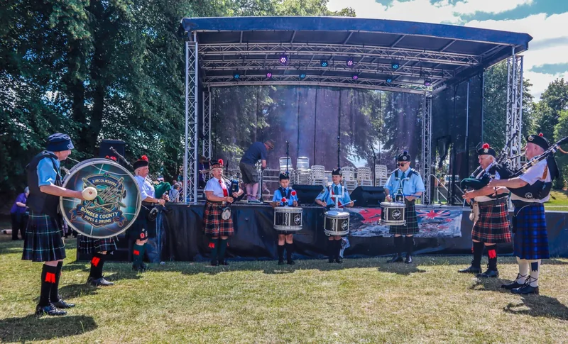 Pipers and drummers performing in front of a festival stage