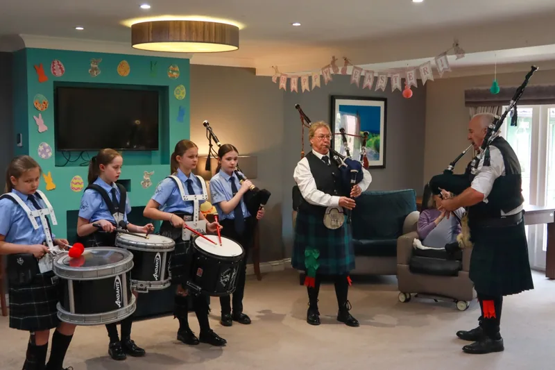 Young drummers and pipers performing for residents in a care-home lounge